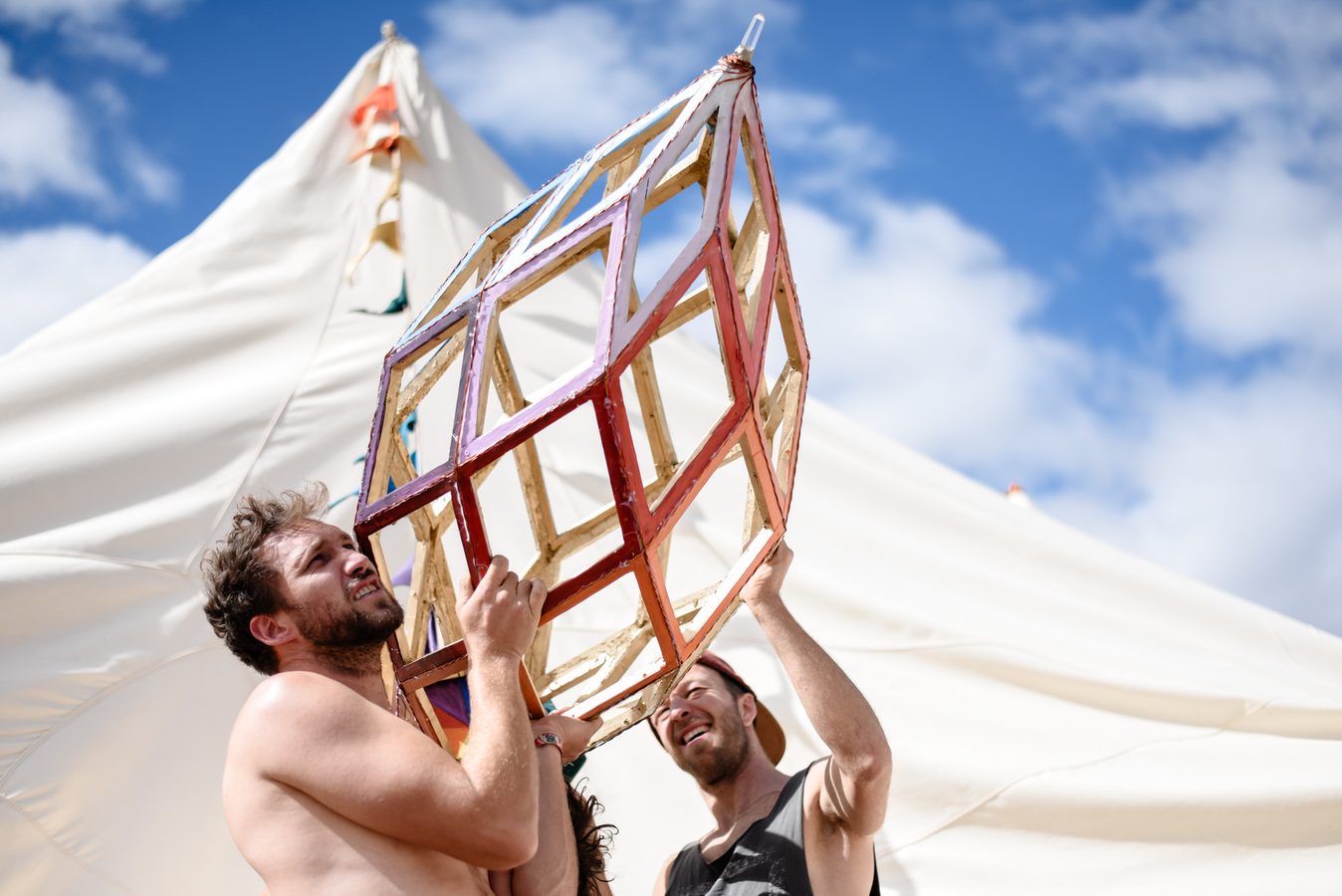 Two builders lifting a coloured lattice finial up to the top of a tent