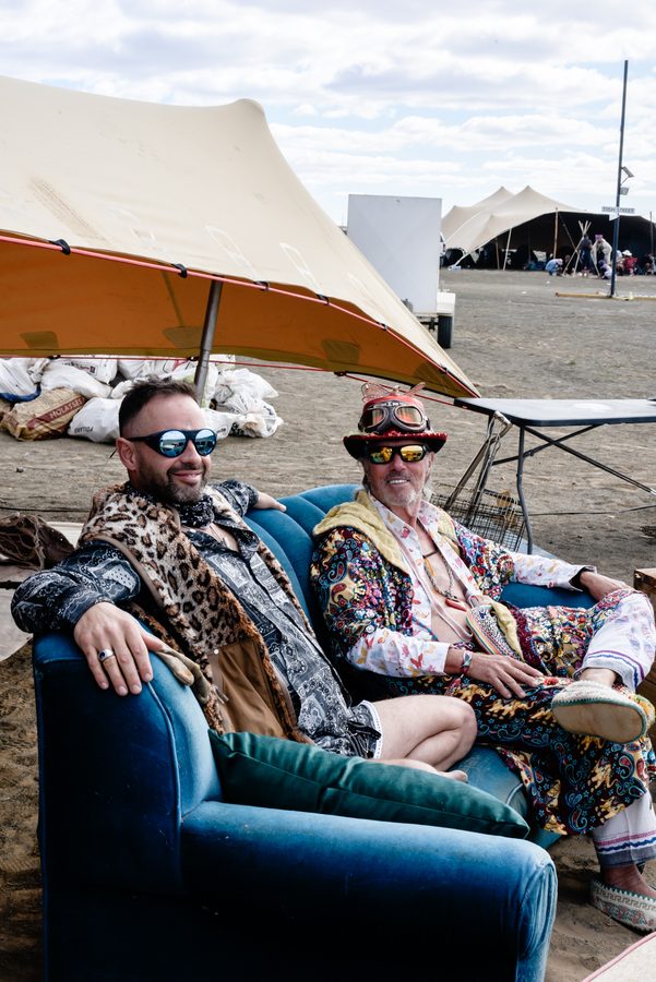 Two camp mates in costume relaxing on a blue sofa in the shade