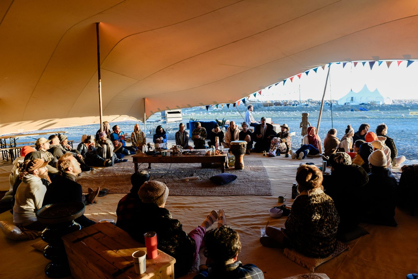 A circle of people sitting under the shade tent in golden light