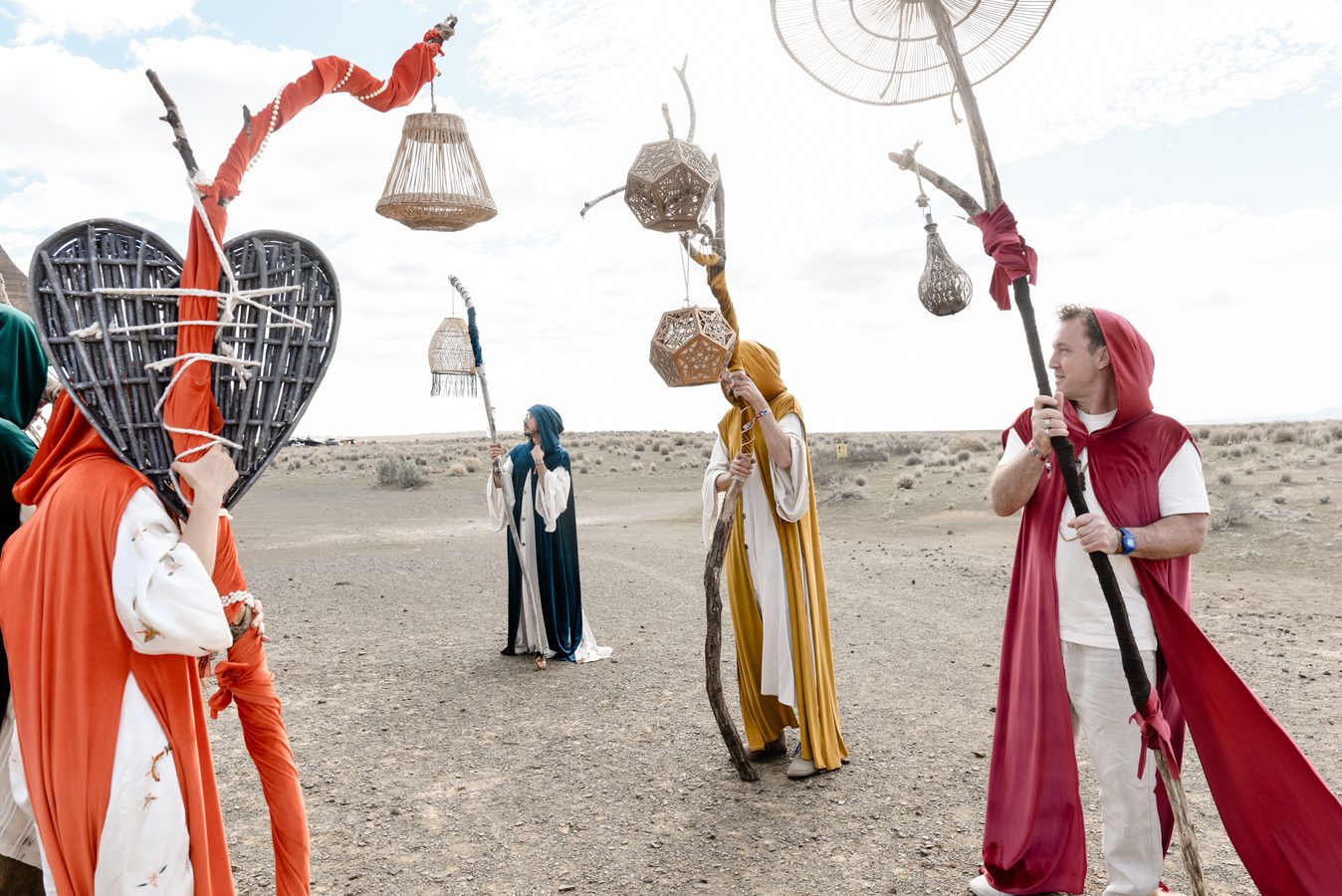 A procession of robed figures carrying staffs and lanterns across the playa