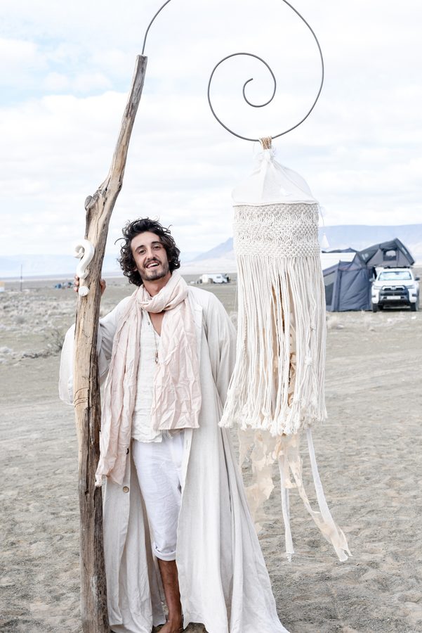 A figure in white holding a tall spiral staff hung with macrame